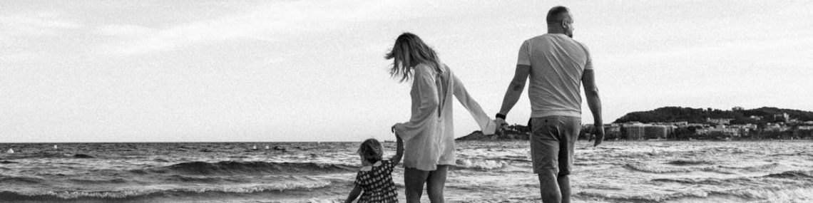 A family enjoys a peaceful walk along the beach with gentle waves.